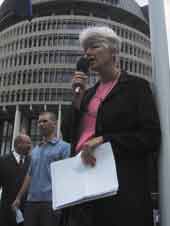 Photo shows Jeanette Fitzsimons speaking with Parliament's beehive in the background. 