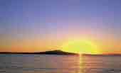 Photo of a sunrise appearing over an island and sea. 