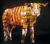 Photo shows a full sized sculpture of a cattle beast made from corned beef cans. 