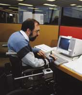 Photo of male worker in a wheelchair at his office work station. 