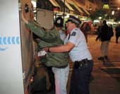 Photo shows a male with his hands against a police vehicle while a police officer searched the man's pockets. 