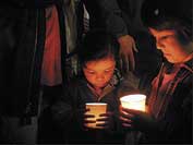 Photo shows two children looking at their lighted candles during a peace rally. 