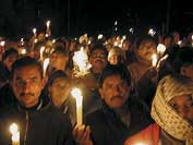 Photo shows large group of people standing holding candles at nighttime peace rally. 